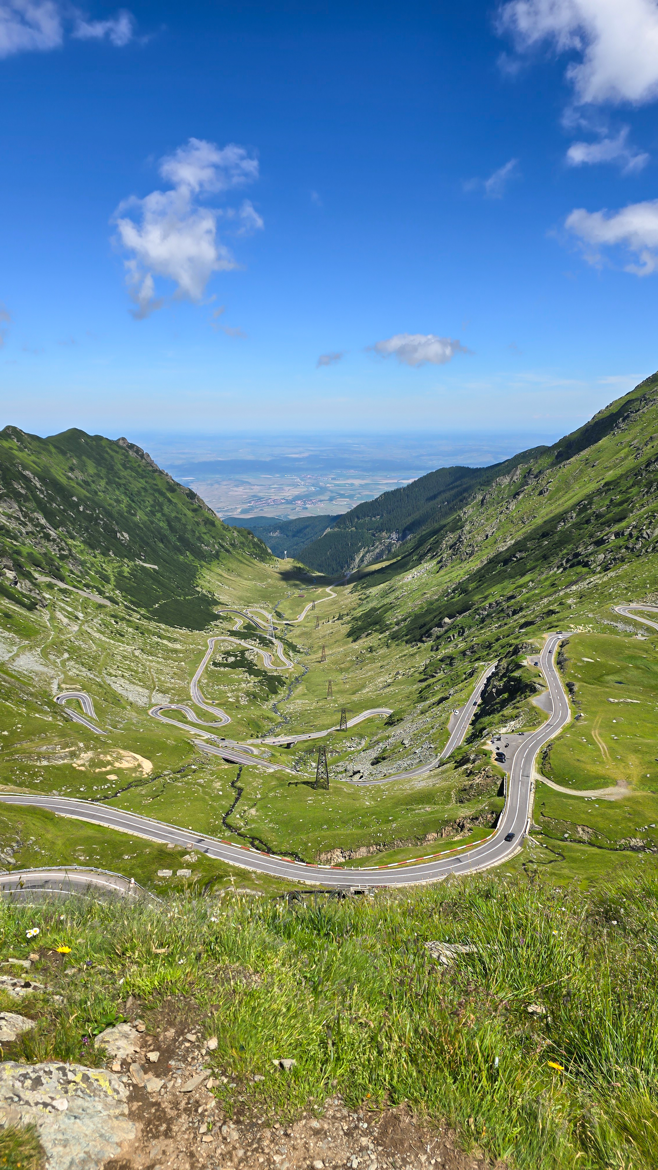 Panoramatický pohled na klikatící se silnici Transfăgărășan v horské krajině, zachycený z vrcholu silnice na šířku.
