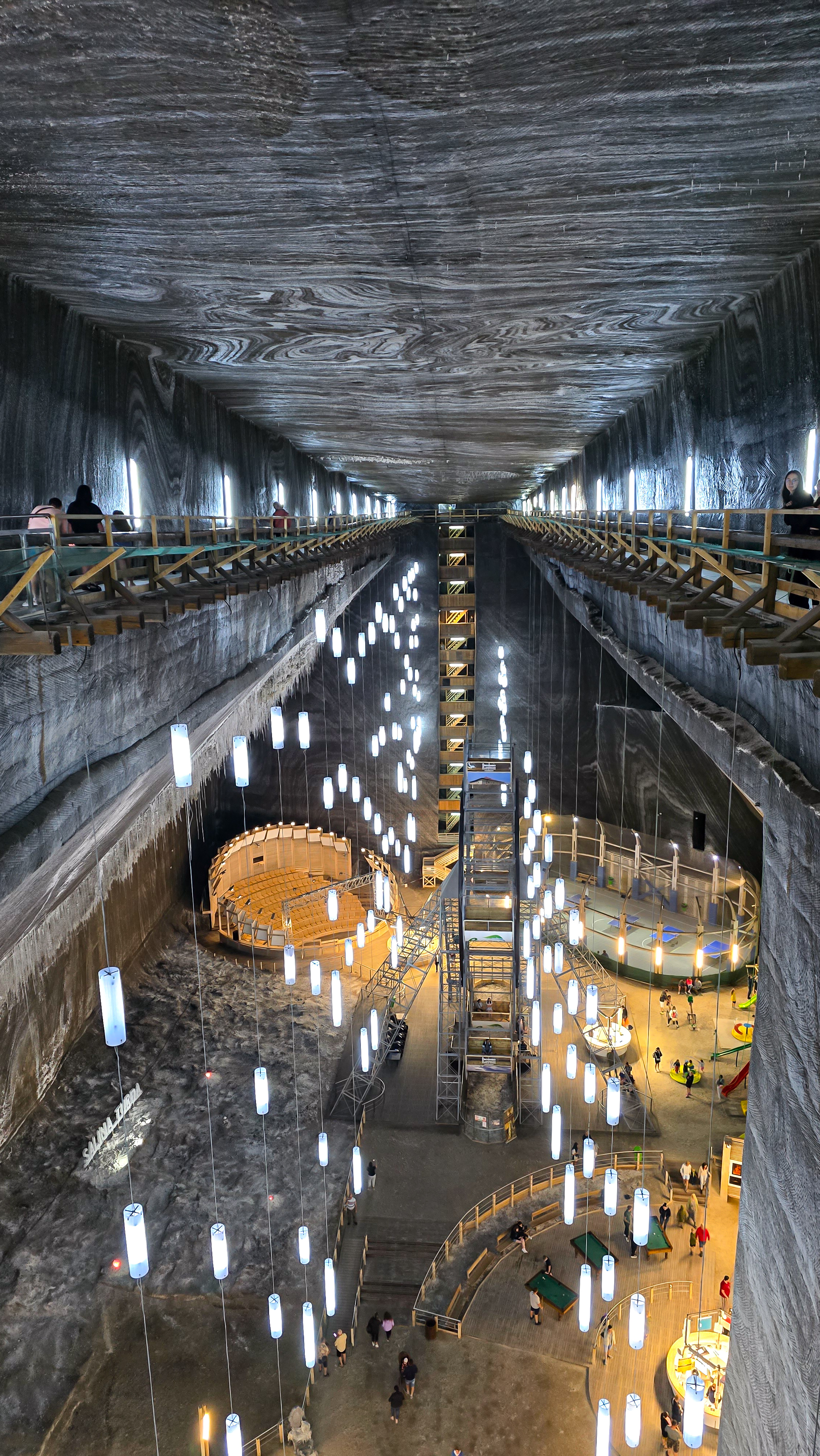 Panoramatický pohled na Rudolfovu šachtu v solném dole Salina Turda – podzemní prostor s modře osvětlenými stěnami a ikonou na kamenném podstavci.